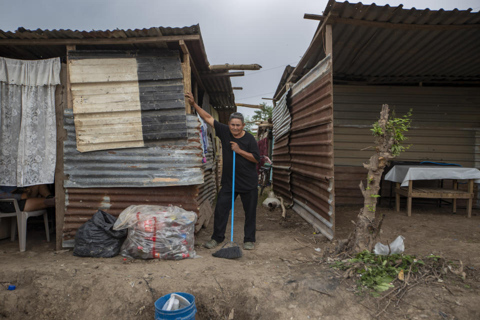 A neighbor pauses as he cleans outside his shack, built after his home was destroyed by last year's hurricanes Eta and Iota in the La Samaritana community of La Lima, on the outskirts of San Pedro Sula, Honduras, Wednesday, Jan. 13, 2021. La Lima has seen small businesses begin to reopen, but in outlying neighborhoods, the streets are still full of debris, dead animals, snakes and burning mattresses. (AP Photo/Moises Castillo)