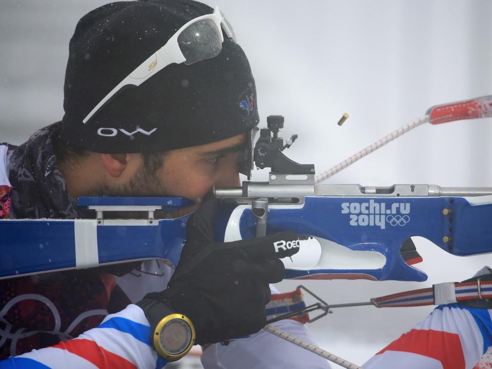 A close up of a man aiming a biathalon gun in the snow