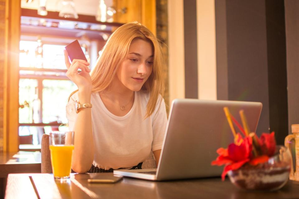 Young adult woman at laptop holding credit card