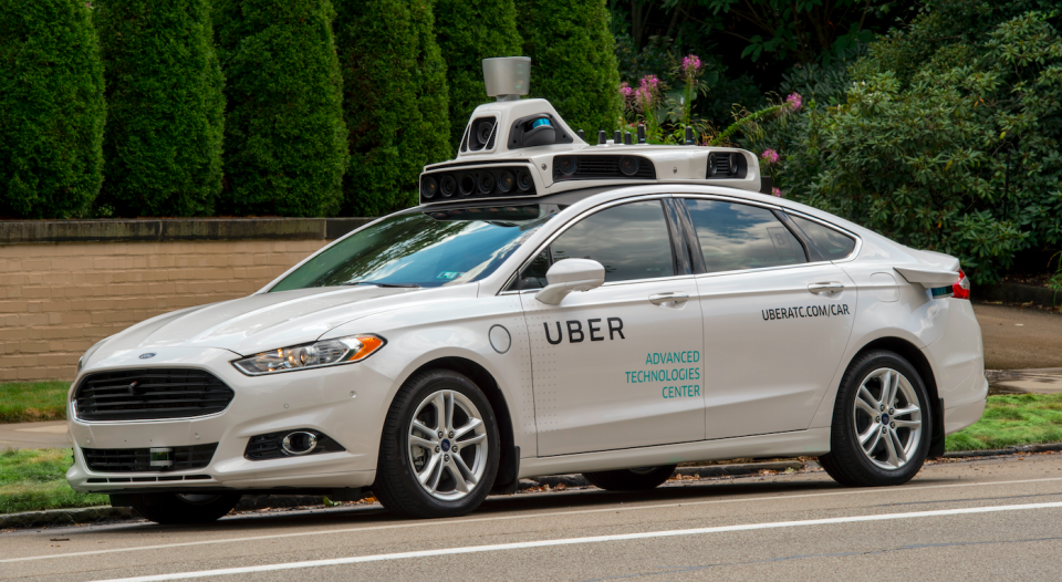 White car with Uber logo on side and self-driving equipment on the roof.