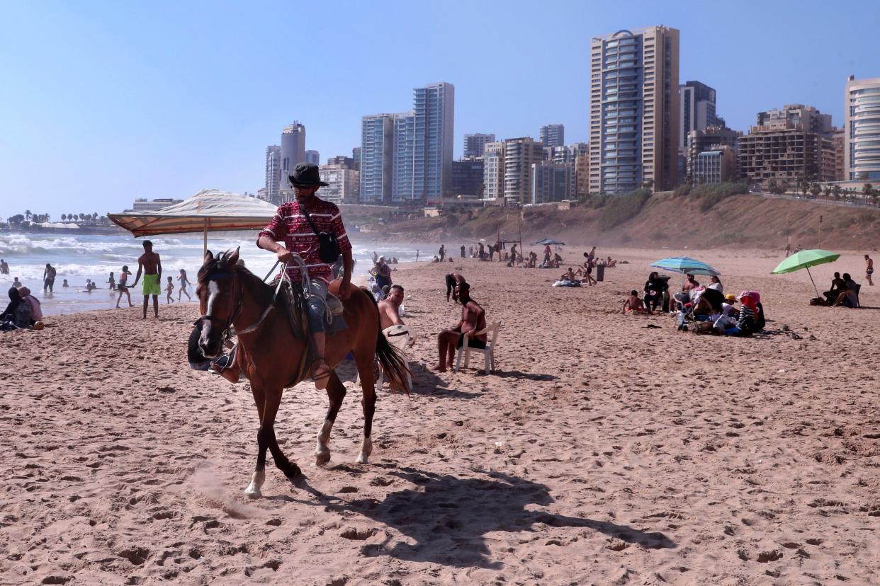 A man rides his horse while people swim in the Mediterranean Sea at Ramlet al-Baida public beach in Beirut, Lebanon on Saturday, June 20, 2020. Lebanon, which has had relatively low numbers of coronavirus infections and is suffering an unprecedented economic and financial crisis, has eased lockdown restrictions and reopened almost all businesses including beaches, pools, restaurants and cafes.