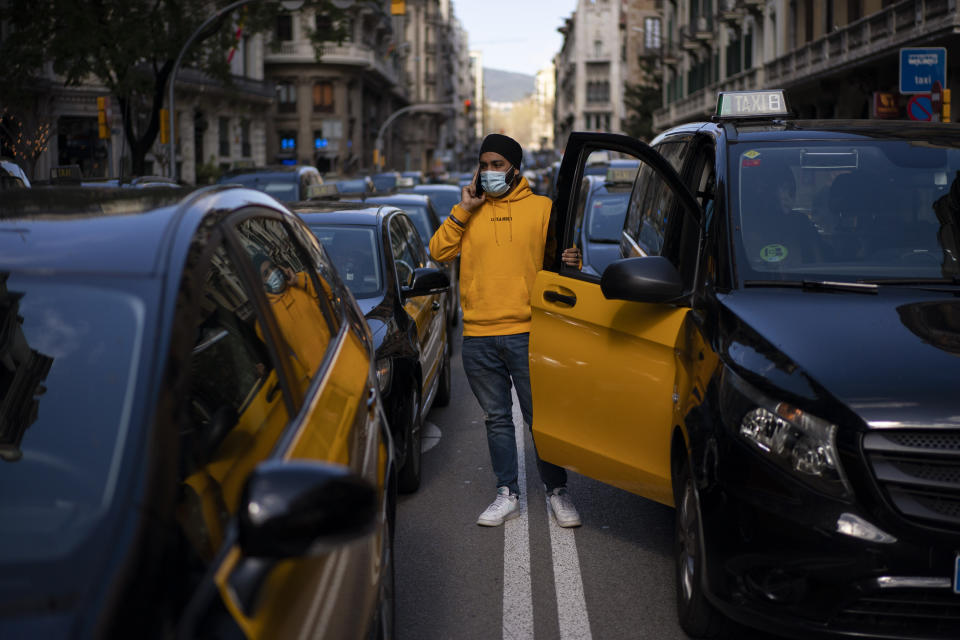 A taxi driver stands next to his cab as they march slowly blocking the traffic along one of the avenues in Barcelona downtown, Spain, Thursday, March 18, 2021. Hundreds of yellow-and-black cabs disrupted Barcelona's road traffic on Thursday to protest against the return of the ride-hailing giant Uber to the northeastern city after a 2-year hiatus. (AP Photo/Emilio Morenatti)