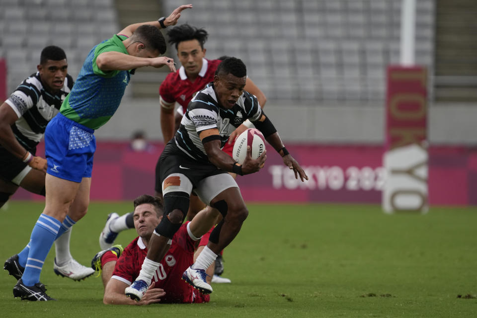 Fiji's Napolioni Bolaca, center, is tackled by Canada's Pat Kay in their men's rugby sevens match at the 2020 Summer Olympics, Monday, July 26, 2021 in Tokyo, Japan. (AP Photo/Shuji Kajiyama)