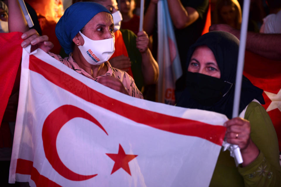 Supporters of the newly elected Turkish Cypriot leader Ersin Tatar hold a Turkish Cypriot breakaway flag and celebrate with others, in the Turkish occupied area in the north part of the divided capital Nicosia, Cyprus, Sunday, Oct. 18, 2020. Ersin Tatar, a hardliner who favors even closer ties with Turkey and a tougher stance with rival Greek Cypriots in peace talks has defeated the leftist incumbent in the Turkish Cypriot leadership runoff. (AP Photo/Nedim Enginsoy)