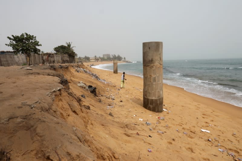 A resident walks along the beach next to the remains of wells that have been exposed in Baguida