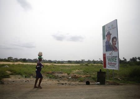 A woman selling groundnut, walks past a billboard campaigning for Nyesom Wike, People's Democratic Party candidate in River state, along a road in Mbiama village, the border town between Nigeria's Bayelsa and River states February 28, 2015. REUTERS/Akintunde Akinleye