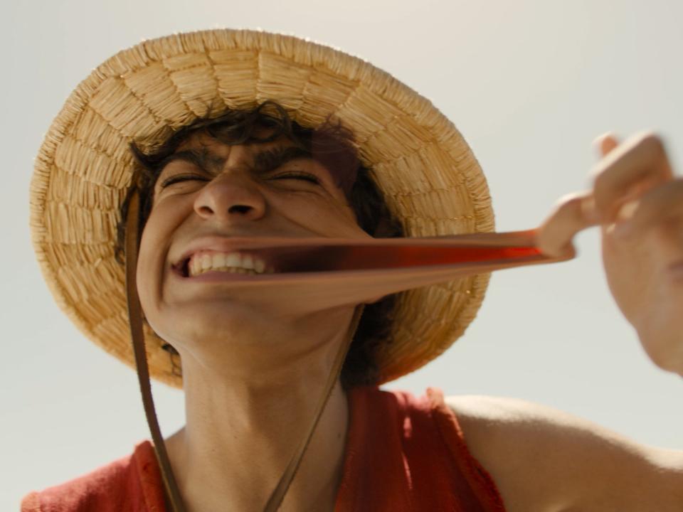 iñaki godoy as luffy in netflix's one piece. he's stretching out his cheek, demonstrating that he can stretch like rubber, and grinning widely