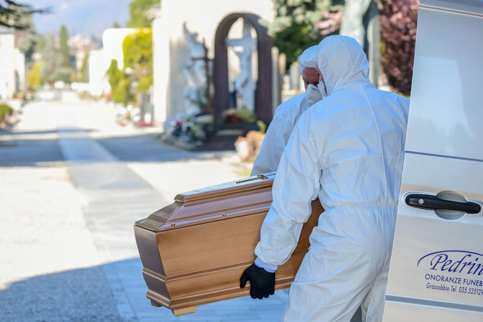 Undertakers wearing a face mask and overalls unload a coffin out of a hearse on March 16, 2020 at the Monumental cemetery of Bergamo, Lombardy, as burials of people who died of the new coronavirus are being conducted at the rythm of one every half hour. (Photo by Piero Cruciatti / AFP) (Photo by PIERO CRUCIATTI/AFP via Getty Images)