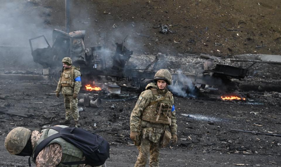 Ukrainian service members surveying the ground amid debris and still-burning fires.