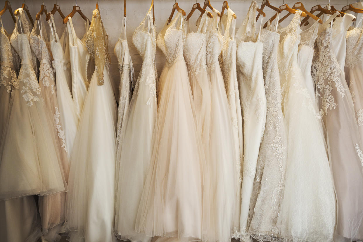 Rows of wedding dresses on display in a specialist wedding dress shop. A variety of colour tones and styles, fashionable lace and boned bodices. 