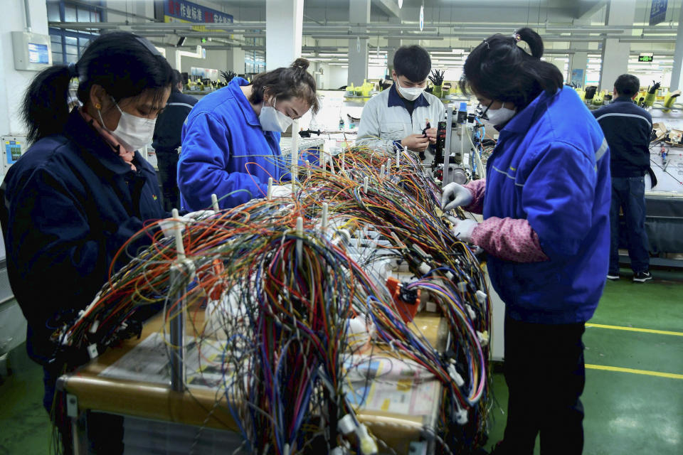 In this Feb. 13, 2020, photo, masked workers assemble wiring for automobile at a factory in Qingdao in east China's Shandong province. Automakers are gradually reopening factories in China that were idled by anti-virus controls as they try to reverse a sales slump in their biggest market. (Chinatopix via AP)