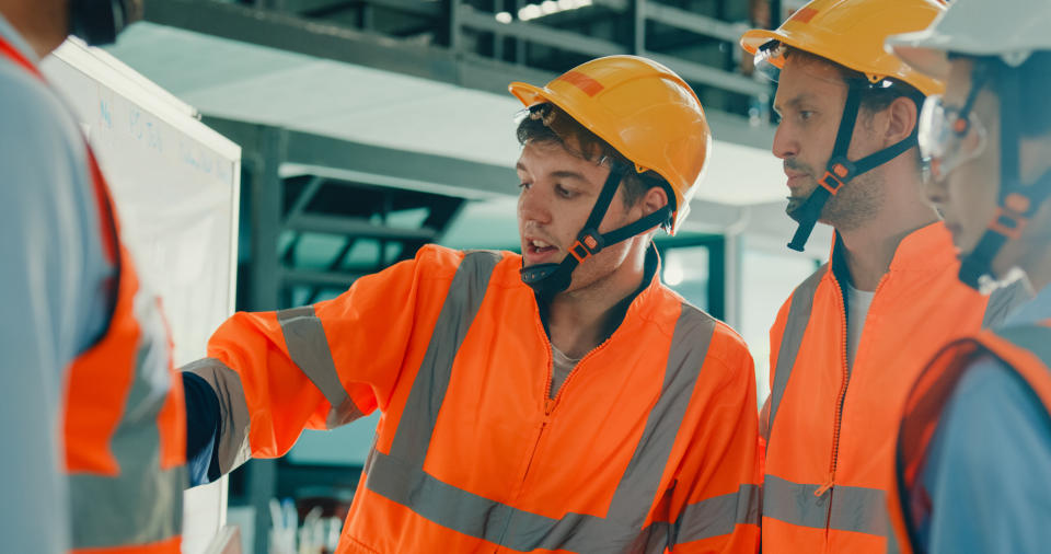 Three construction workers in safety gear discussing over a blueprint at a work site