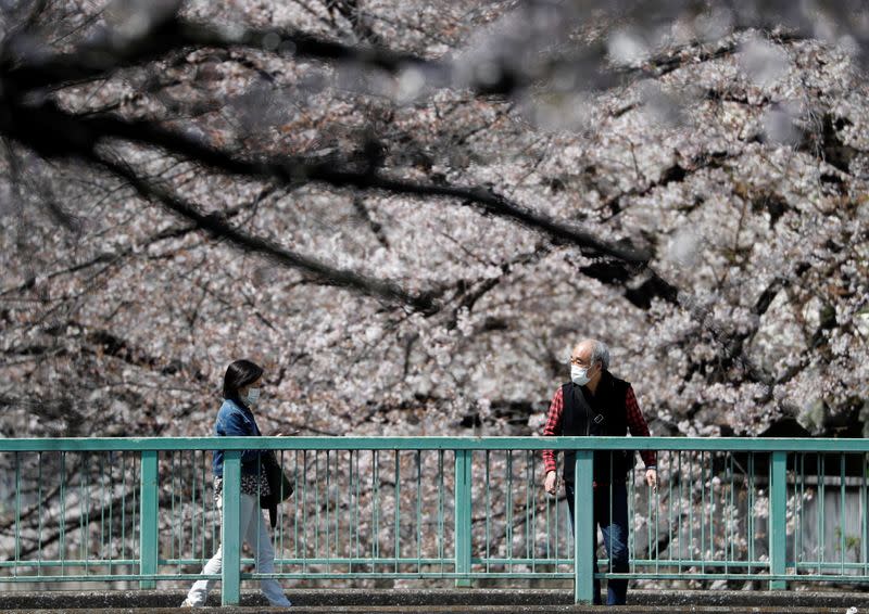 Passersby wearing protective face masks look at blooming cherry blossoms amid the coronavirus disease (COVID-19) pandemic, in Tokyo