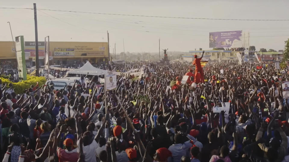 Bobi Wne speaking on top of a car in the middle of a huge crowd.