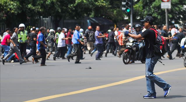 In this photo released by China's Xinhua News Agency, an unidentified man with a gun walks in the street as people run in the background on Thamrin street near Sarinah shopping mall in Jakarta, Indonesia. Photo: AP