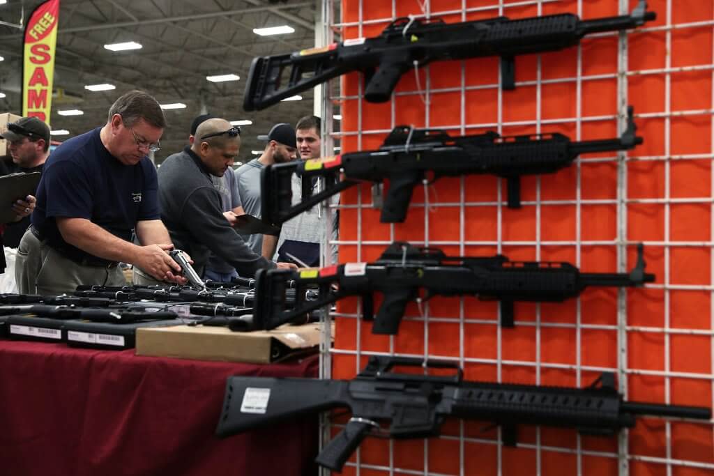 Potential buyers try out guns which are displayed on an exhibitor’s table at a gun show