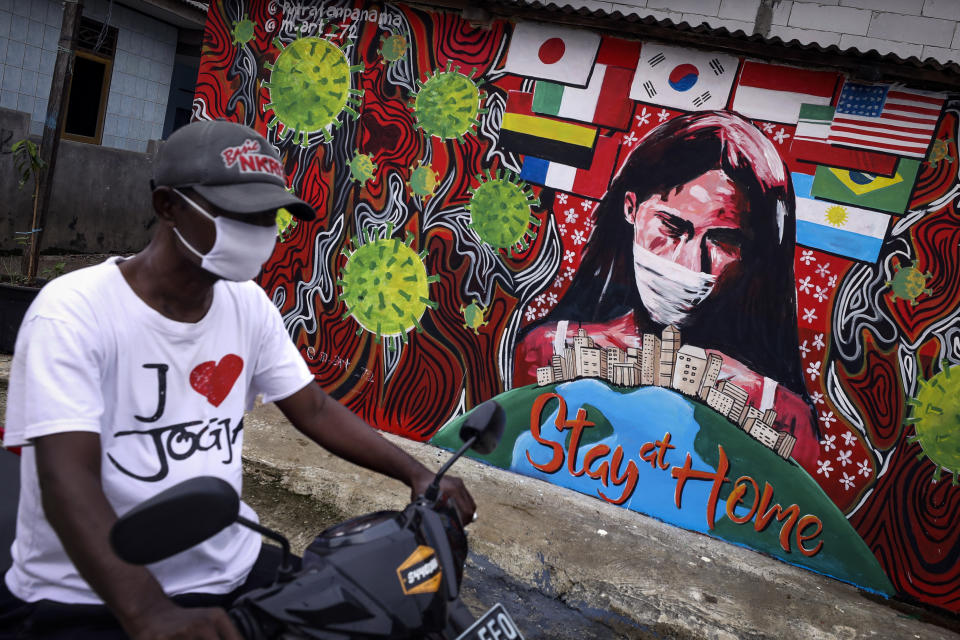 A motorist wearing a face mask rides past a coronavirus themed mural in Depok on the outskirts of Jakarta, Indonesia, Wednesday, April 15, 2020. (AP Photo/Dita Alangkara)