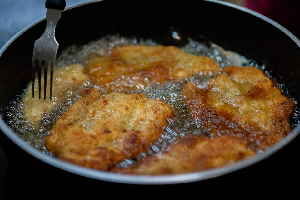 Close-up of breaded chicken pieces frying in a pan, with a fork lifting one piece