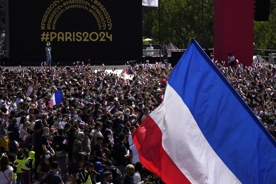 A fan waves the French flag in the Olympics fan zone at Trocadero Gardens in front of the Eiffel Tower in Paris, Sunday, Aug. 8, 2021. A celebration was held in Paris Sunday as part of the handover ceremony of Tokyo 2020 to Paris 2024, as Paris will be the next Summer Games host in 2024. The passing of the hosting baton will be split between the Olympic Stadium in Tokyo and a public party and concert in Paris. (AP Photo/Francois Mori)