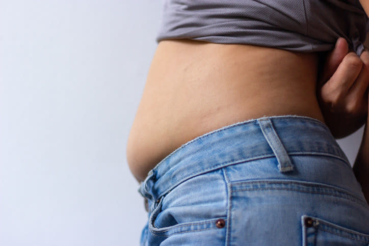 A stomach spreading over a jeans waist slightly