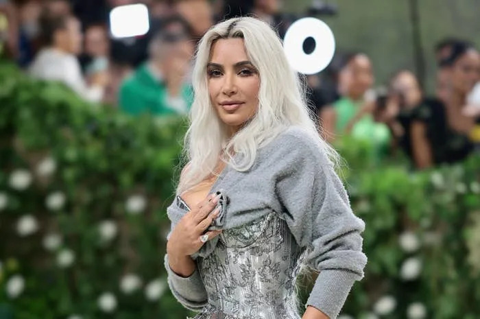 Kim Kardashian wearing an off-the-shoulder top and a metallic corset dress at an event with a floral backdrop