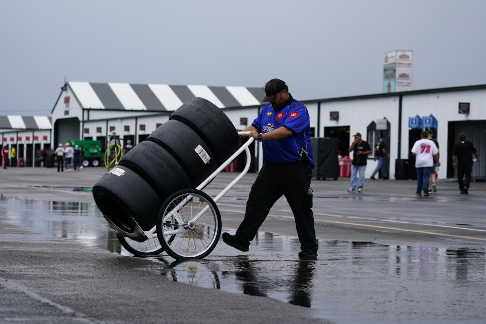 A crew member crosses a puddle with a cart of tires after a rain storm cancelled practice and qualifying for Saturday's NASCAR Truck Series auto race at Pocono Raceway, Friday, July 22, 2022, in Long Pond, Pa. (AP Photo/Matt Slocum)