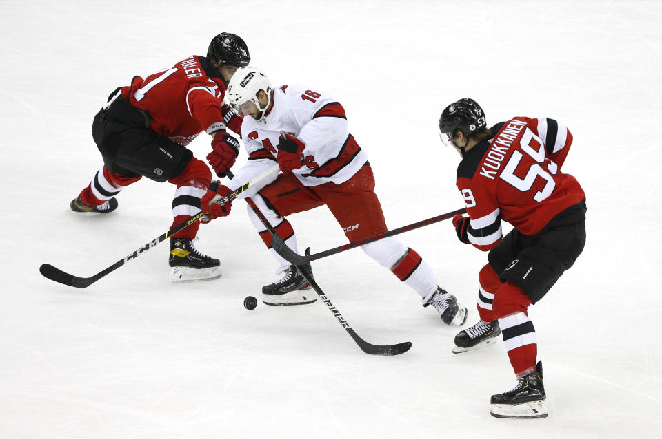 Carolina Hurricanes center Vincent Trocheck (16) plays the puck against New Jersey Devils defenseman Jonas Siegenthaler (71) and center Janne Kuokkanen (59) during the third period of an NHL hockey game, Saturday, Jan. 22, 2022, in Newark, N.J. (AP Photo/Noah K. Murray)