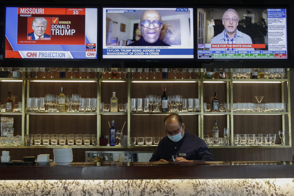 A waiter works under television sets that show U.S. presidential election reports at a restaurant in Taguig, Philippines, Wednesday, Nov. 4, 2020. (AP Photo/Aaron Favila)