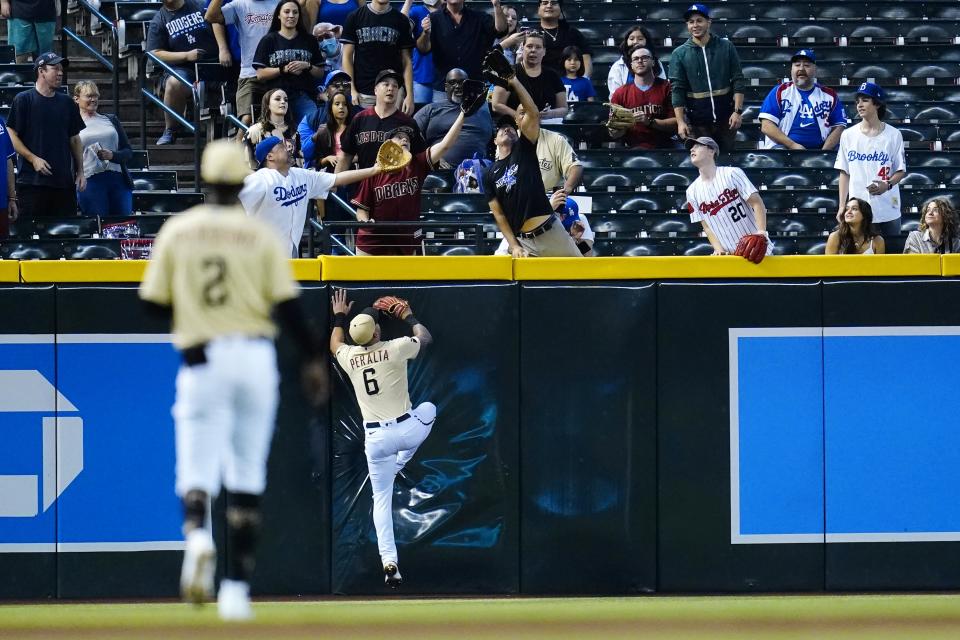 Arizona Diamondbacks left fielder David Peralta (6) and shortstop Geraldo Perdomo (2) watch fans reach for a home run hit by Los Angeles Dodgers' Trea Turner during the first inning of a baseball game Sunday, Sept. 26, 2021, in Phoenix. (AP Photo/Ross D. Franklin)