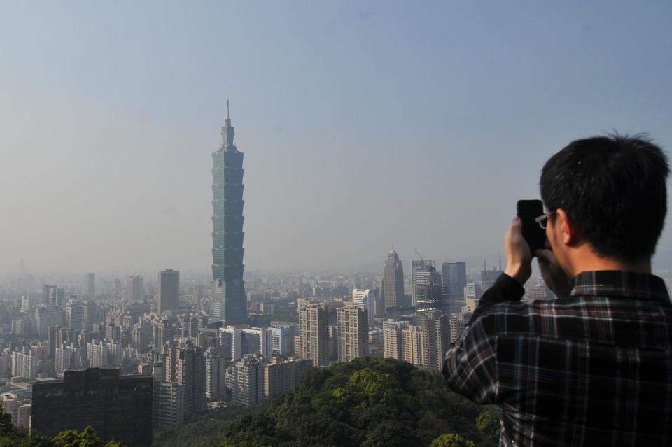 A tourist taking photos of Tower 101 as a haze of pollution sits over the city's skyline on a clear day in Taipei on Feb. 25, 2013.