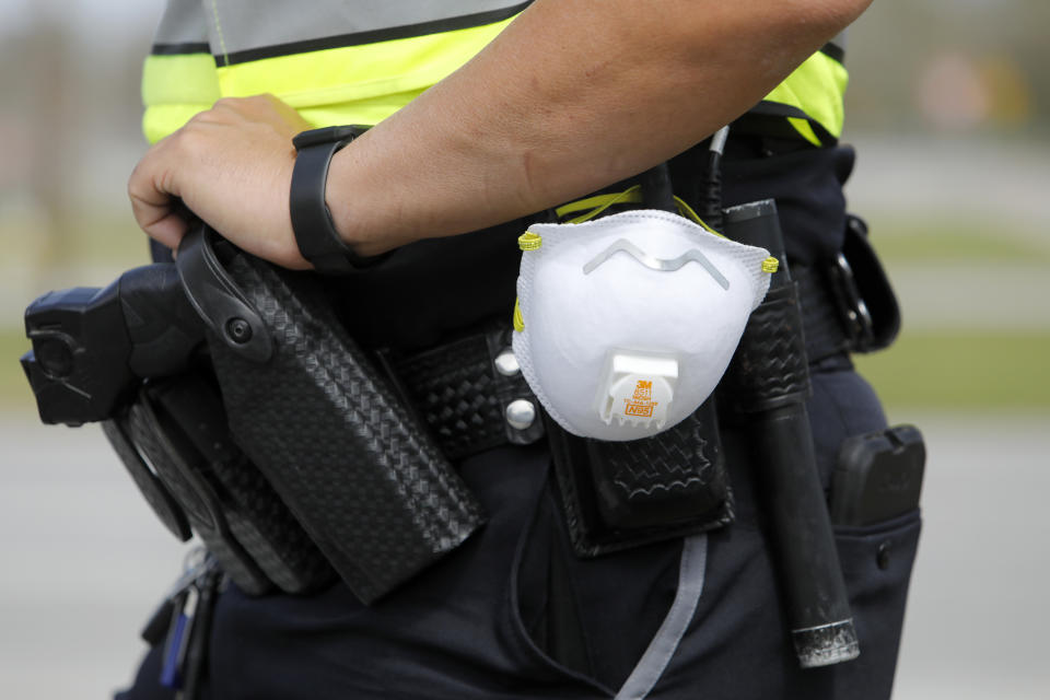 In this March 16, 2020, photo a North Charleston police officer carries a protective mask around his gun belt while working traffic at Roper St. Francis' North Charleston office in North Charleston, S.C. The coronavirus has the potential to profoundly change law enforcement in the U.S. as police departments are shifting resources and changing how they police while the virus strikes. (AP Photo/Mic Smith, File)