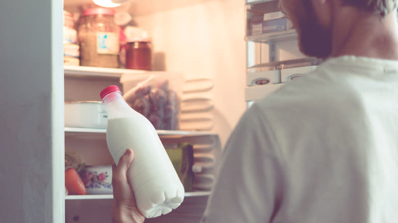 man grabbing bottled milk from fridge