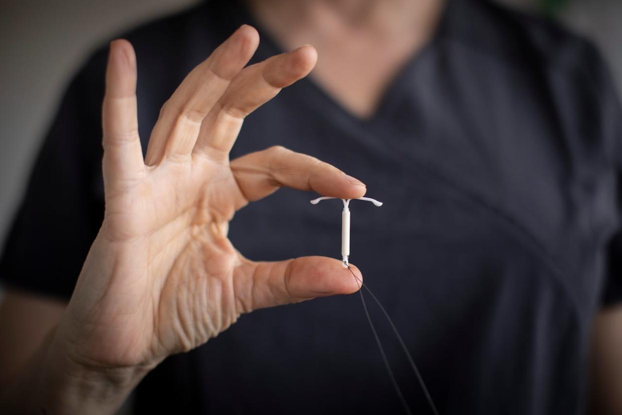 Dr. Renee Hall, medical co-director at Willow Clinic, holds an IUD in her hand. She says a new fee structure from the province has allowed her to hire four new doctors, which will help shorten the wait list for IUD insertion.   (Ben Nelms/CBC - image credit)