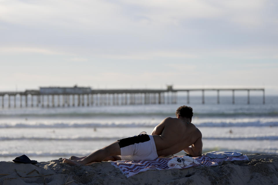 Vernon Benton relaxes on a towel in front of the Ocean Beach pier, Tuesday, Jan. 30, 2024, in San Diego. Rising seas, frequent storms take toll on California's iconic piers, threatening beach landmarks. (AP Photo/Gregory Bull)