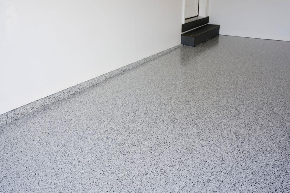 A wide view of grey terrazzo flooring with black stairs in the background.
