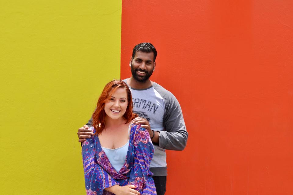 the wrtier and her partner posing in front of a yellow and orange wall