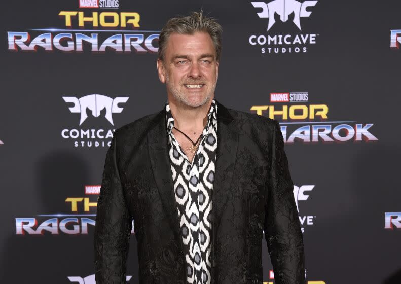 Ray Stevenson in a dark blazer and a patterned dress shirt smiling at a red carpet
