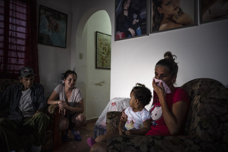 Marialys Gonzalez Lopez cries as she holds her granddaughter Madisson during an interview at their home in Havana, Cuba, Tuesday, Dec. 6, 2022, one week before her two daughters and granddaughter left to migrate to the U.S. At left is Madisson's great-grandfather, Alejandro Gonzalez Lopez, and aunt Merlyn. (AP Photo/Ramon Espinosa)