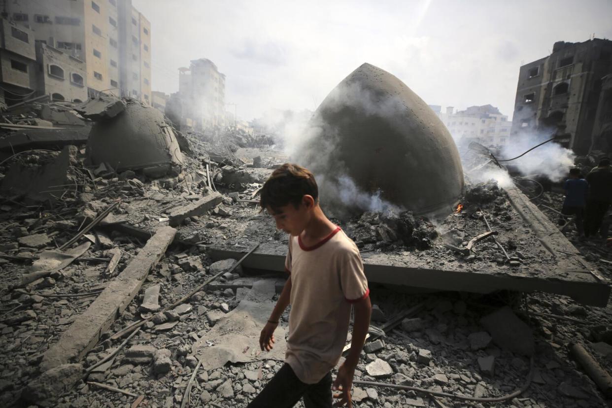 A person walks amid rubble and the smoking remains of a building