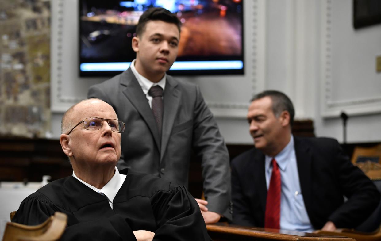 Judge Bruce Schroeder, left, comes down from the bench and sits closer to a  television screen to watch an evidence video as Kyle Rittenhouse, center, and his attorney Mark Richards stand watch behind him during proceedings at the Kenosha County Courthouse on Friday.