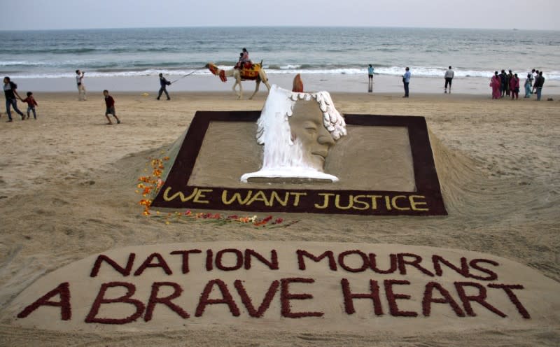 People walk near a sand sculpture with the words "We Want Justice" created by Indian sand artist Sudarshan Patnaik, in solidarity with a gang rape victim who was assaulted in New Delhi, on a beach in the eastern Indian state of Odisha