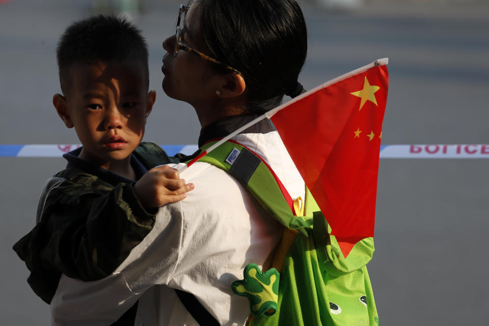 A woman carries a child with a national flag wait behind a police barricade line as residents watch Chinese military vehicles and floats in preparation for the parade for the 70th anniversary of the founding of the People's Republic of China, in Beijing, Tuesday, Oct. 1, 2019. (AP Photo/Andy Wong)