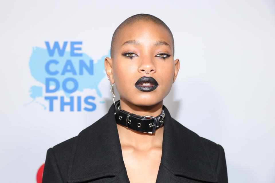 Person with a choker and black outfit, posing in front of a 'We Can Do This' backdrop