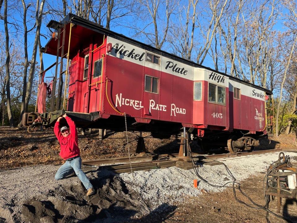 Ray Devite in a red sweatshirt hangs off the front of the Nickel Plate Caboose