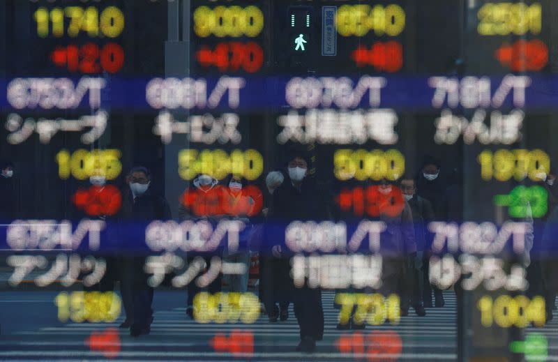 FILE PHOTO: Pedestrians wearing protective masks are reflected on an electronic board outside a brokerage in Tokyo