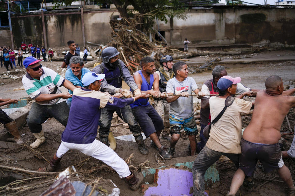 Local residents and relief workers pull a rope to remove wreckage in search for survivors from a home destroyed by flooding caused by heavy rains in Las Tejerias, Venezuela, Sunday, Oct. 9, 2022. At least 22 people died after intense rain overflowed a ravine causing flash floods, Vice President Delcy Rodríguez said. (AP Photo/Matias Delacroix)