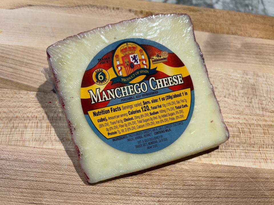 White wedge of cheese with red casing with blue and yellow label reading "Manchego cheese"