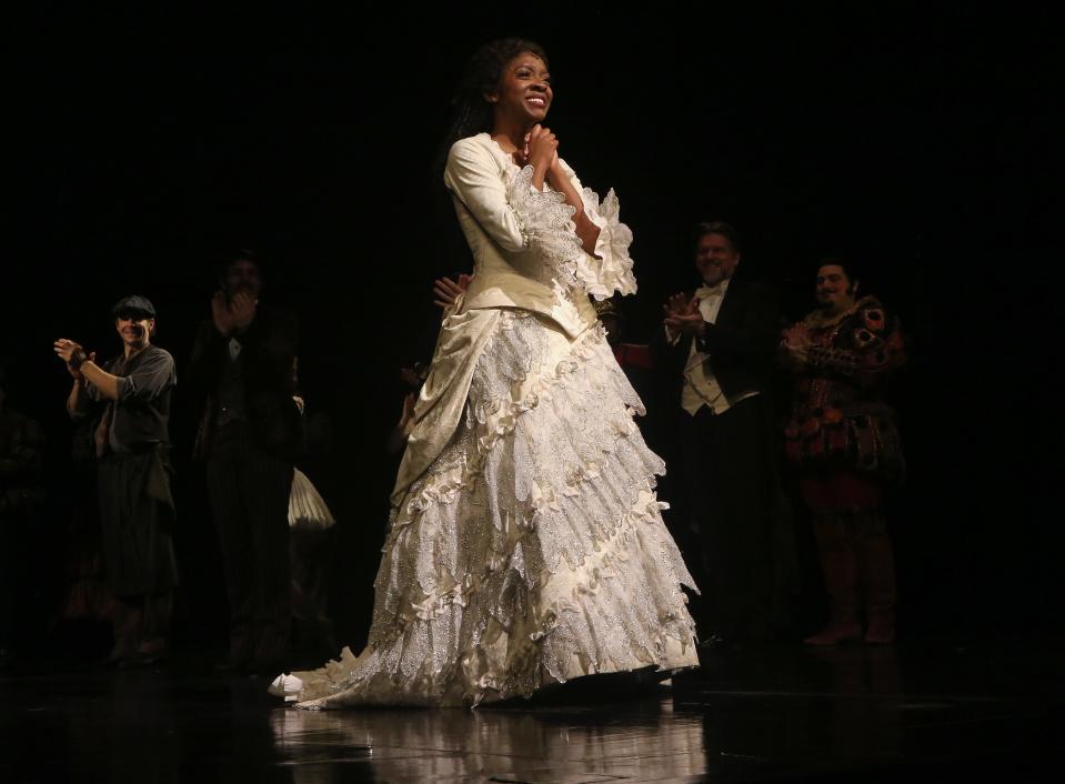 Emilie Kouatchou in costume as she clasps her hands under her chin onstage