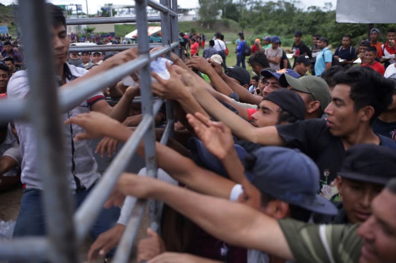 Migrants from Central America, part of a caravan travelling to the U.S., grab water as they wait to cross into Mexico at the border between Guatemala and Mexico, in El Ceibo