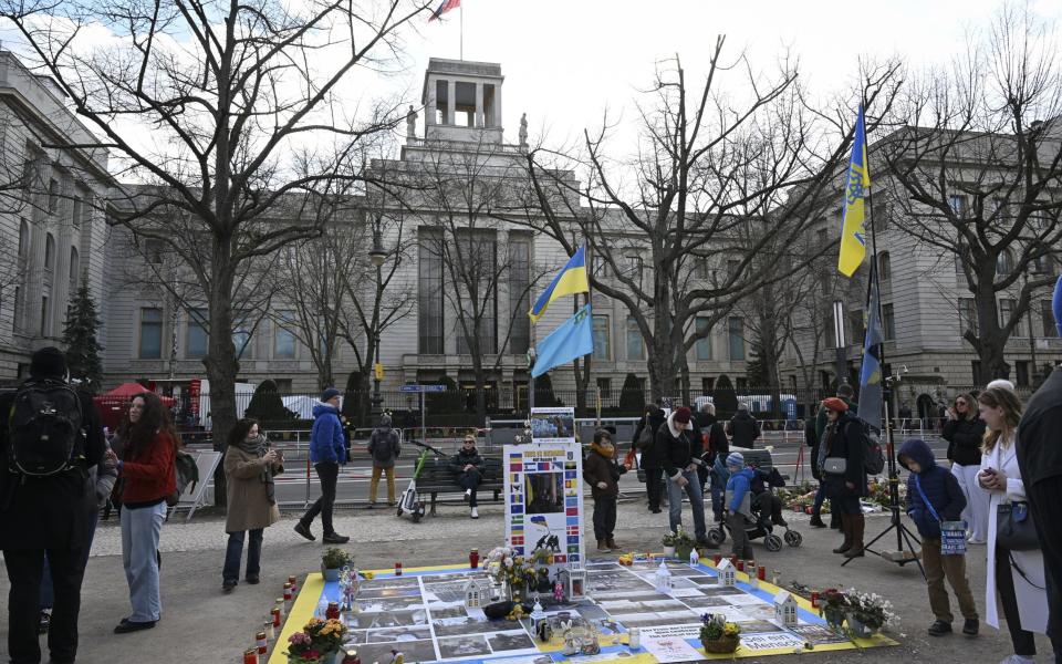 The embassy is a large, imposing, grey building in the Soviet style. There are trees in front of it and a few protesters flying Ukrainian flags and displaying printed material about the war